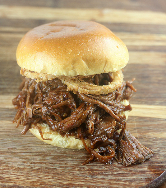 BBQ pulled beef sandwich with crispy onions on a wooden board