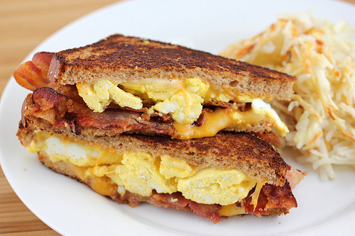 Breakfast grilled cheese with bacon, egg, and cheese on a plate with hash browns