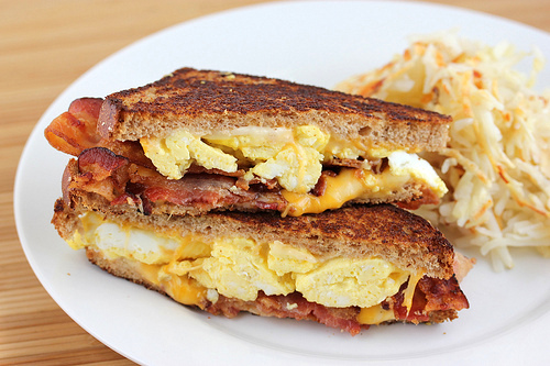 Breakfast grilled cheese with bacon, egg, and cheese on a plate with hash browns