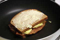 Breakfast grilled cheese sandwich cooking in a pan with bacon and egg