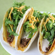 Cheesy gordita crunch tacos filled with seasoned beef, lettuce, cheese, and sauce on a white plate