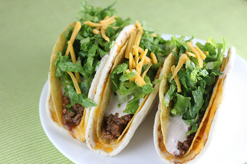 Cheesy gordita crunch tacos filled with seasoned beef, lettuce, cheese, and sauce on a white plate