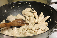 Chicken pieces cooking in a wok with a wooden spoon