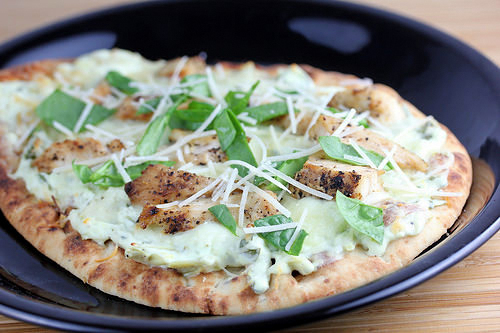 Flatbread pizza topped with grilled chicken, spinach, artichoke spread, and shredded parmesan