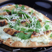 Flatbread pizza topped with grilled chicken, spinach, artichoke spread, and shredded parmesan