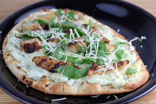 Flatbread pizza topped with grilled chicken, spinach, artichoke spread, and shredded parmesan