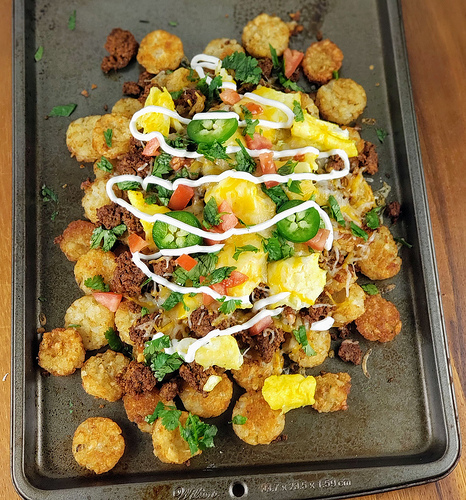 Loaded chorizo totchos with eggs and melted cheese on a tray