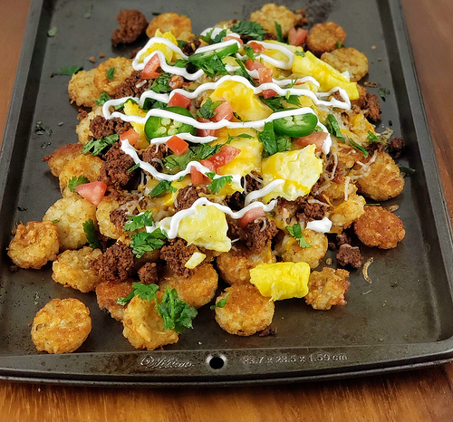 Chorizo totchos topped with scrambled eggs, and sour cream on a baking sheet