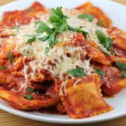 Ravioli topped with melted cheese and fresh parsley on white plate