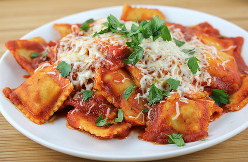 Plate of cheesy ravioli with tomato sauce and parsley