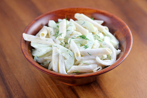Wooden bowl filled with creamy cucumber pasta salad topped with dill