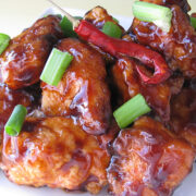 Plated General Tso’s chicken piled high with green onions and a whole red chili pepper
