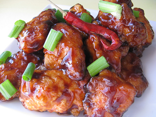 Plated General Tso’s chicken piled high with green onions and a whole red chili pepper