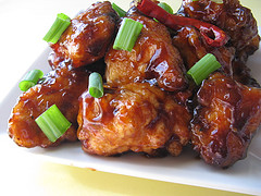 Close-up of saucy General Tso’s chicken with green onions on a white plate