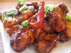 General Tso’s chicken garnished with green onions and a red chili pepper on a white plate