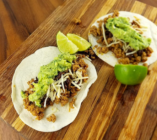 Two ground pork tacos topped with guacamole and shredded cheese