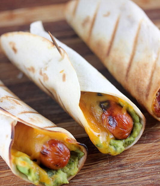 Hot dog tacos wrapped in tortillas with cheddar and guacamole