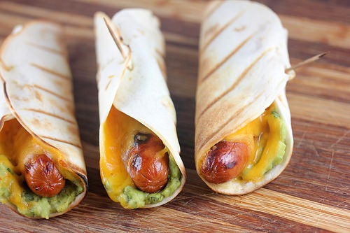 Grilled hot dogs with melted cheese and guacamole in tortillas