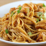 Plate of kung pao linguine topped with chicken and peanuts