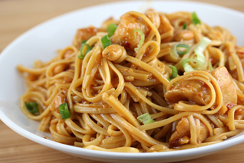 Plate of kung pao linguine topped with chicken and peanuts
