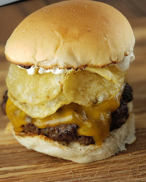 Close-up of burger stacked with cheddar cheese, potato chips, and mayonnaise