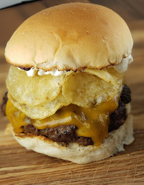 Close-up of burger stacked with cheddar cheese, potato chips, and mayonnaise