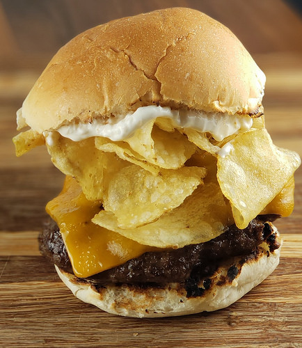 Cheeseburger topped with potato chips and mayonnaise on a wooden board