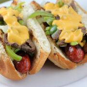 Close-up of Philly cheese steak hot dogs loaded with beef, peppers, onions, and cheese sauce