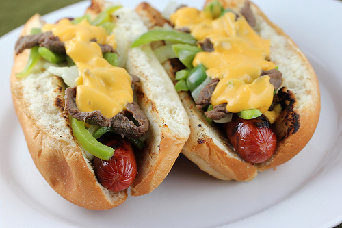 Close-up of Philly cheese steak hot dogs loaded with beef, peppers, onions, and cheese sauce