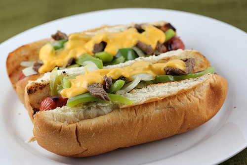 Philly cheese steak hot dogs topped with onions, green peppers, and melted cheese sauce