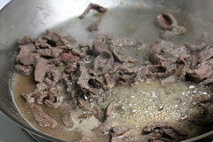 Sliced beef cooking in a skillet with bubbling juices