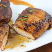 Juicy spice-rubbed pork chops on a white plate with one piece sliced to show tenderness