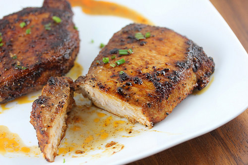 Juicy spice-rubbed pork chops on a white plate with one piece sliced to show tenderness