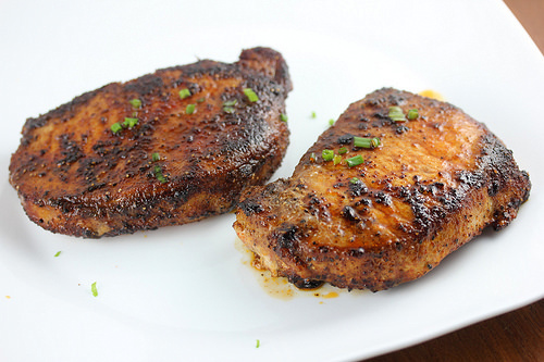 Seared pork chops seasoned with spice rub and garnished with chopped chives on a white plate