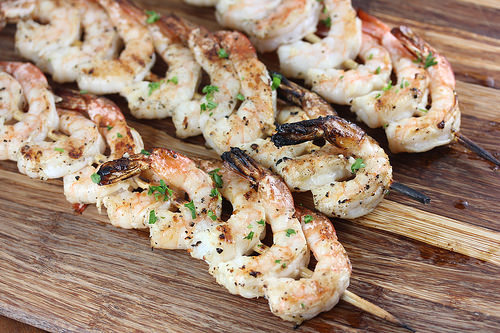 Grilled shrimp skewers on a wooden board, lightly charred and garnished with herbs