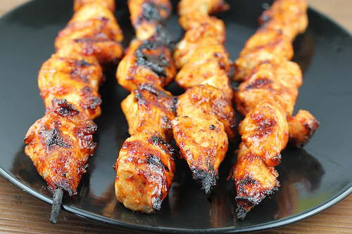 Grilled spicy chicken skewers on a black plate