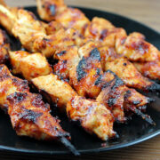 Grilled spicy chicken skewers on a black plate