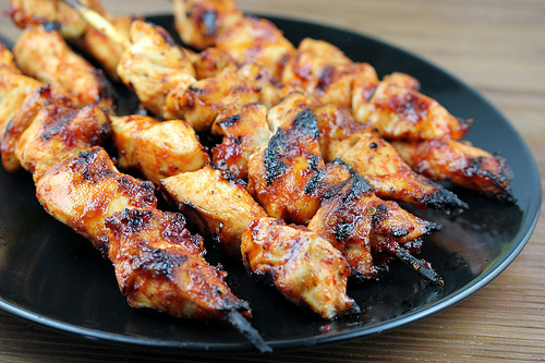 Grilled spicy chicken skewers on a black plate