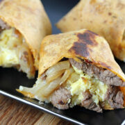 Grilled tortilla wrap filled with steak, eggs, and cheese on a black plate