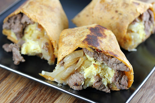 Grilled tortilla wrap filled with steak, eggs, and cheese on a black plate