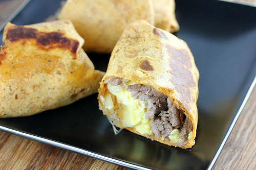 Grilled tortilla wrap filled with steak, eggs, and cheese on a black plate