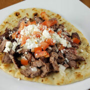 Steak gyro with diced tomatoes, onions, feta cheese, and sauce on flatbread