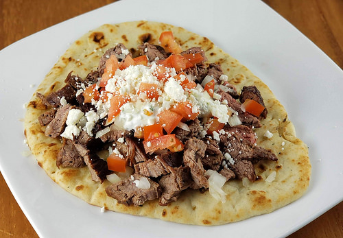 Steak gyro with diced tomatoes, onions, feta cheese, and sauce on flatbread