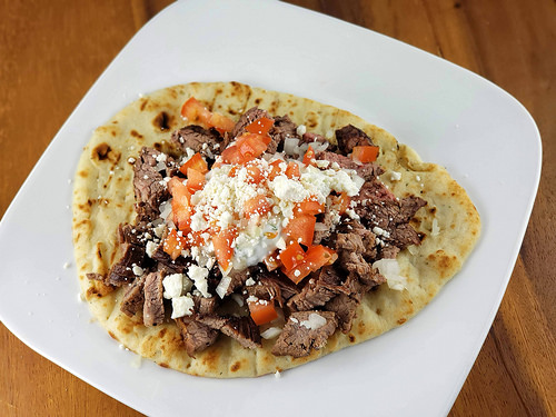 Steak gyro with diced tomatoes, onions, feta cheese, and sauce on flatbread