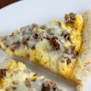Slice of breakfast pizza with eggs, sausage, and melted cheese