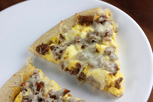 Slice of breakfast pizza with eggs, sausage, and melted cheese