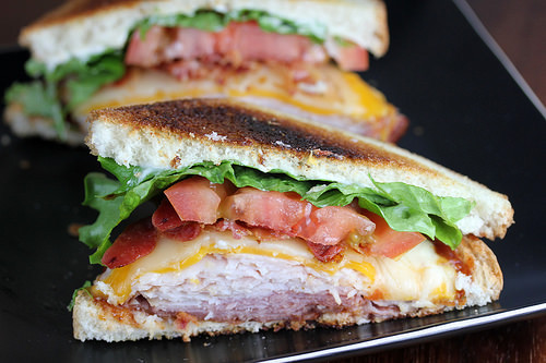 Clubhouse sandwich with turkey, bacon, cheese, lettuce, and tomato on toasted bread