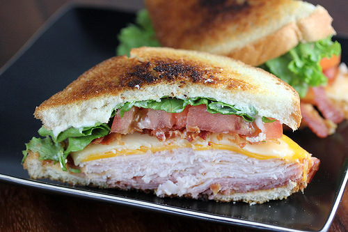 Clubhouse sandwich with turkey, bacon, cheese, lettuce, and tomato on toasted bread