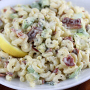 Bacon and avocado pasta salad with creamy dressing and lemon wedge on a white plate
