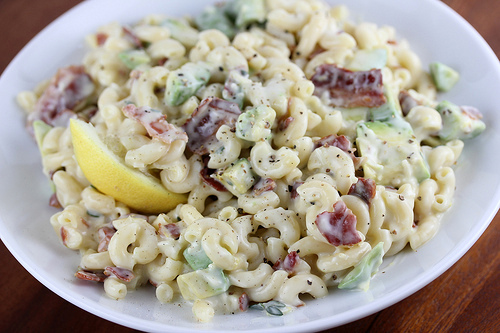 Bacon and avocado pasta salad with creamy dressing and lemon wedge on a white plate